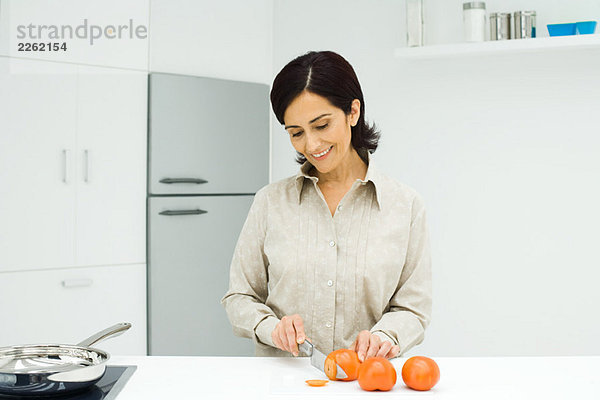 Frau steht an der Küchentheke  schneidet Tomaten mit Messer auf