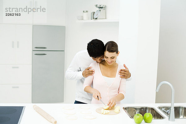 Paar steht zusammen in der Küche  Frau schneidet Äpfel  Mann lehnt Kopf auf der Schulter