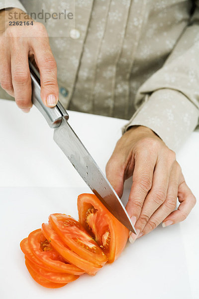 Frau schneidet Tomate mit Messer  Schnittansicht