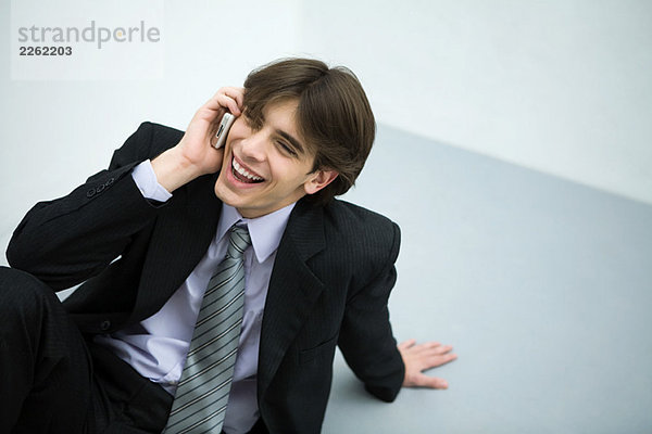 Junger Mann im Anzug auf dem Boden sitzend  Handy benutzend  lächelnd