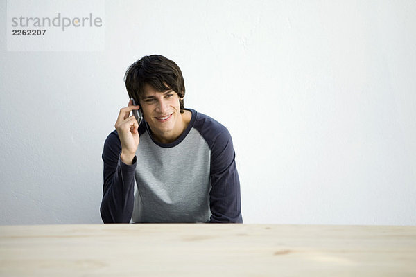 Junger Mann am Tisch sitzend  Handy benutzend  lächelnd