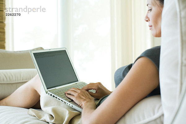 Frau auf dem Sofa sitzend  mit Laptop  Seitenansicht