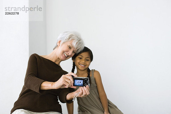 Seniorin fotografiert sich selbst und ihre Enkelin mit Digitalkamera  beide lächelnd.