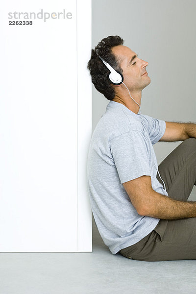 Mann sitzt auf dem Boden  hört Kopfhörer  Augen zu.