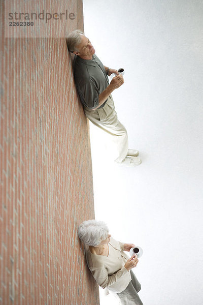 Frau und Mann stehen auseinander  lehnen sich an die Wand  halten Kaffeetassen  hohe Blickwinkel