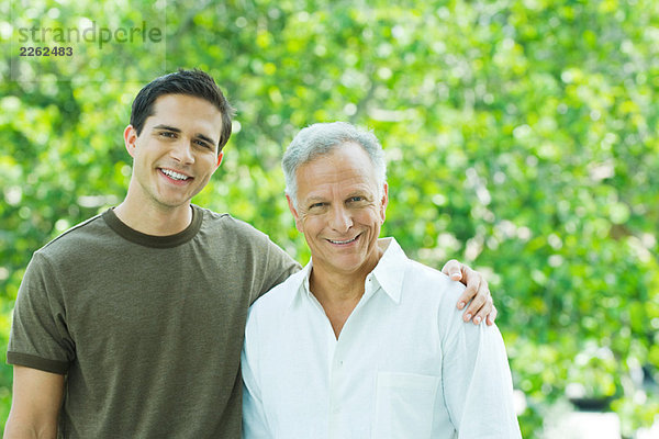 Erwachsener Mann und erwachsener Sohn lächeln gemeinsam vor der Kamera im Freien  Porträt