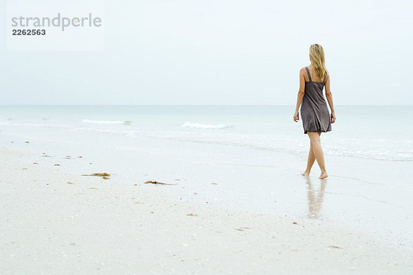 Frau im Sonnenkleid am Strand entlang  Rückansicht