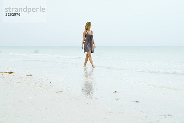 Frau im Sonnenkleid am Strand entlang  Blick auf die Aussicht