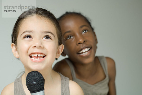 Zwei junge Mädchen  die zusammen ins Mikrofon singen  lächeln und aufschauen