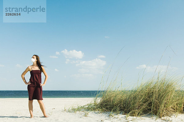 Frau  die am Strand steht und eine Verschmutzungsmaske trägt.