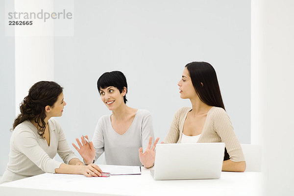 Drei Geschäftsfrauen sitzen am Tisch  diskutieren  eine gestikulieren mit den Händen