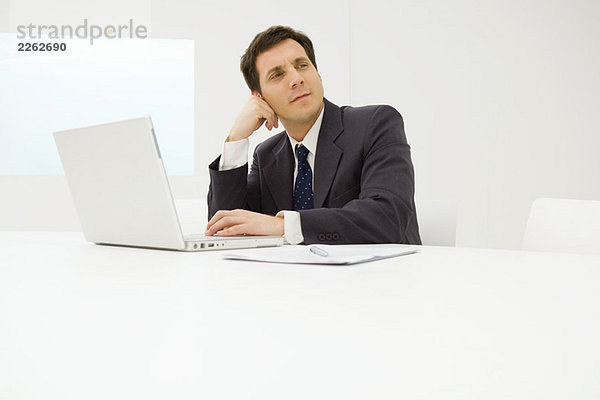 Geschäftsmann mit Laptop am Schreibtisch  Kopf halten  wegschauen