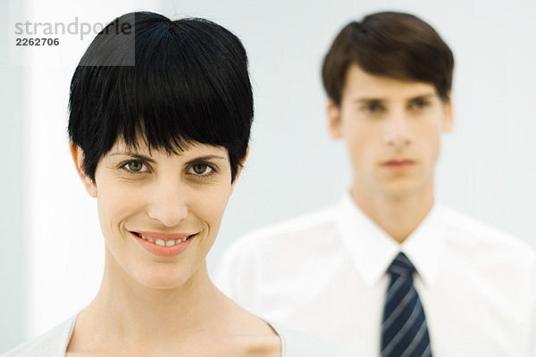 Geschäftsfrau lächelt vor der Kamera  Nahaufnahme  männlicher Kollege im Hintergrund