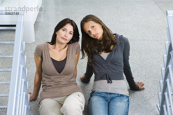 Mutter und Tochter sitzen zusammen auf dem Boden und schauen in die Kamera.