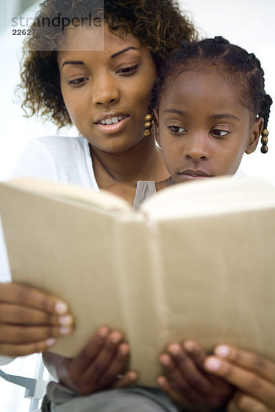 Mutter und Tochter lesen gemeinsam Buch  Mädchen sitzt auf dem Schoß der Frau  Nahaufnahme