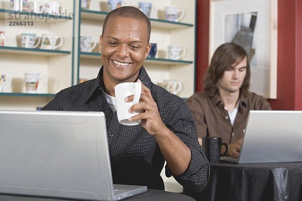 Zwei junge Männer an ihren Laptops in einem Café