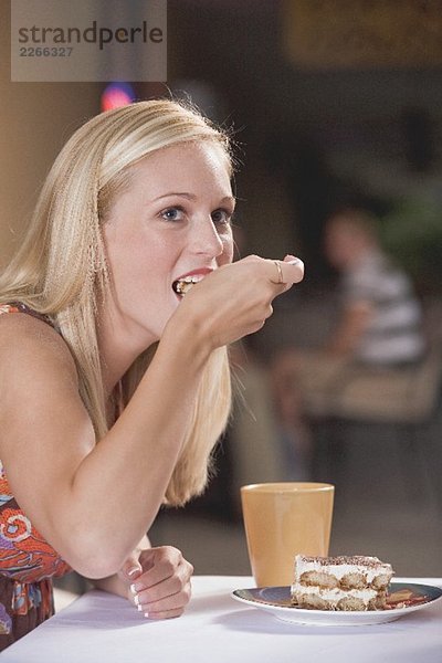 Junge blonde Frau isst ein Stück Tiramisu