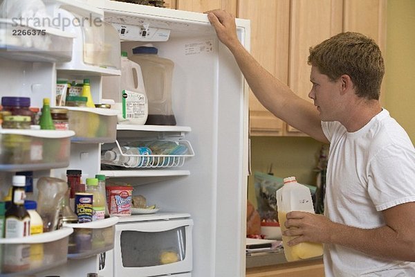 Mann im T-Shirt begutachtet den Inhalt seines Kühlschranks