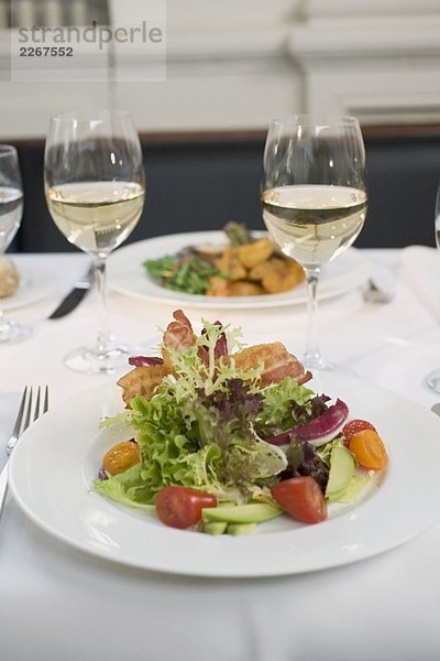 Blattsalat mit Bacon und Weissweingläser auf gedecktem Tisch