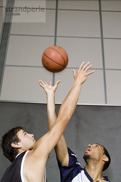 Zwei Basketballspieler  die nach einem Basketball greifen.