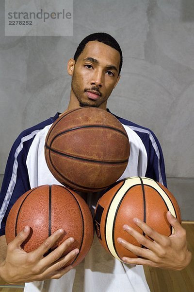 Ein junger Mann mit drei Basketbällen.