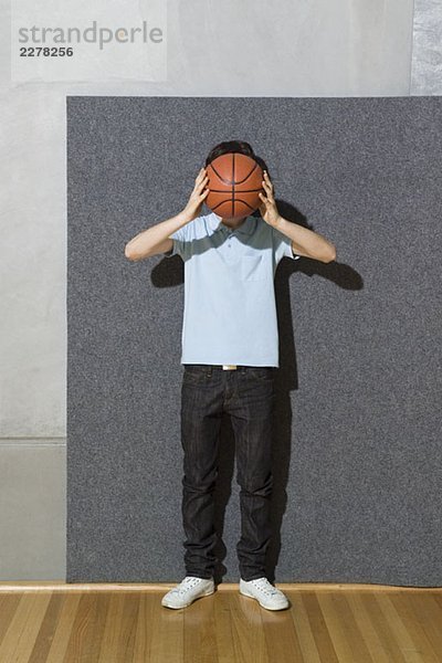 Ein Mann  der einen Basketball vor sein Gesicht hält.