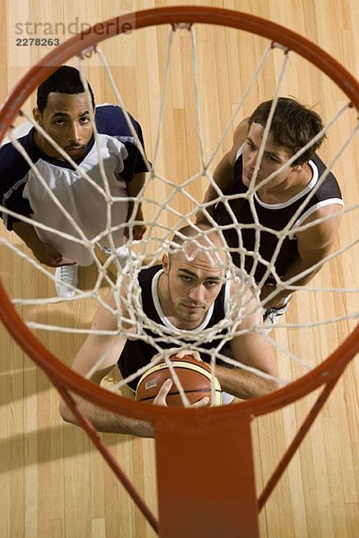 Drei Basketballspieler stehen unter einem Basketballkorb.