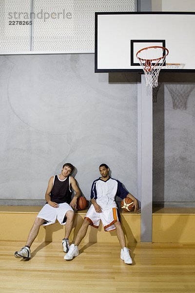 Zwei junge Männer sitzen auf einer Bank auf einem Basketballplatz.