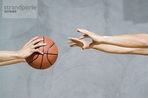 Zwei Sätze menschlicher Arme  die einen Basketball passieren.