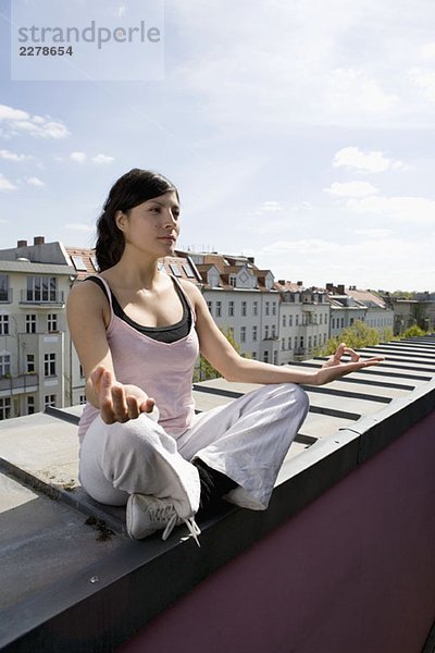 Eine junge Frau  die Yoga auf dem Dach praktiziert.