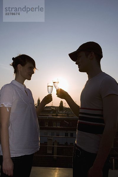 Ein junges Paar  das bei Sonnenuntergang auf einer Dachterrasse mit Champagner anstößt.