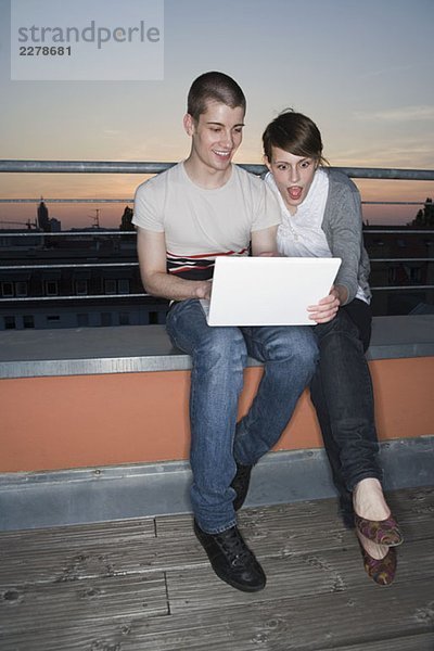 Ein junges Paar mit einem Laptop auf einer Dachterrasse