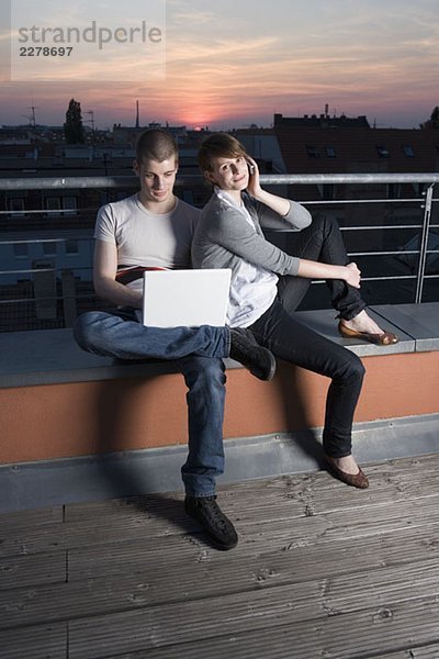 Ein junges Paar mit einem Laptop auf einer Dachterrasse