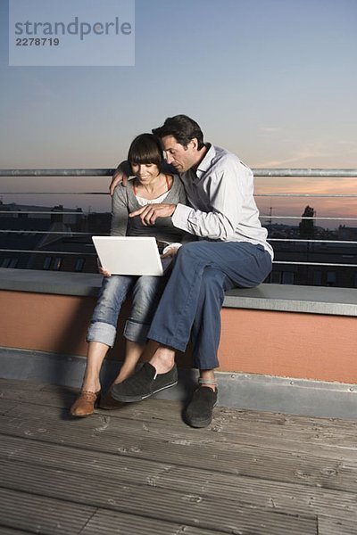 Ein Paar mit einem Laptop auf einer Dachterrasse