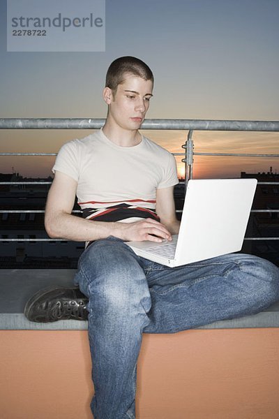 Ein junger erwachsener Mann  der einen Laptop auf einer Dachterrasse benutzt.