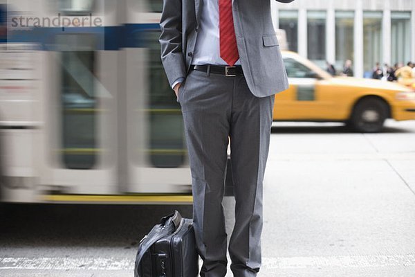 Ein Geschäftsmann  der auf einem Bürgersteig steht und ein Handy benutzt.