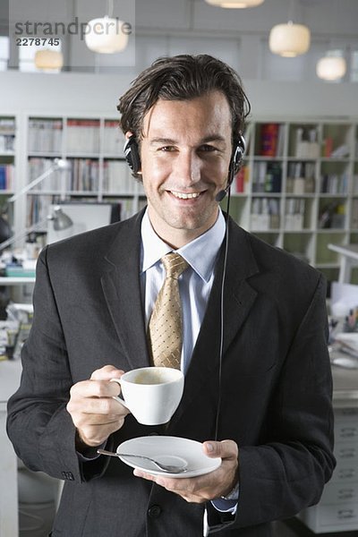 Ein Mann  der ein Telefon-Headset trägt und eine Tasse Kaffee hält.