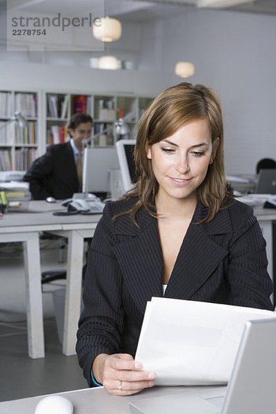 Eine Frau  die sich ein Dokument ansieht  während sie an einem Schreibtisch im Büro sitzt.