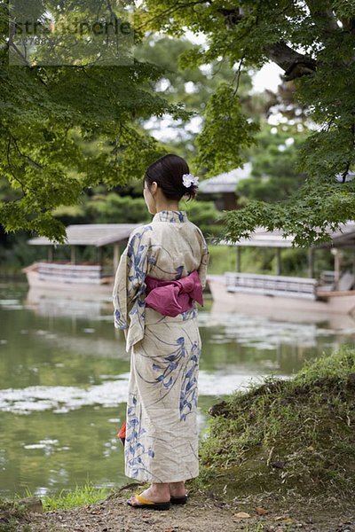 Eine Frau mit Kimono  die am Ufer eines Sees steht.