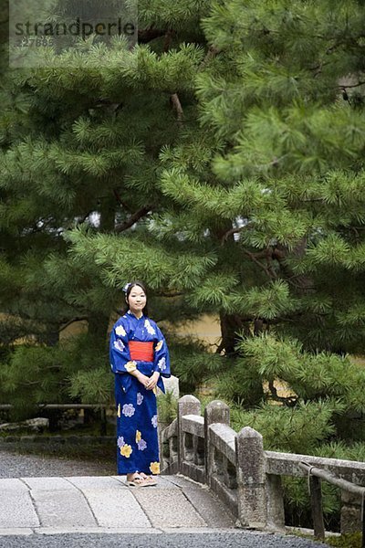 Eine Frau  die einen Kimono trägt  steht auf einer Brücke.