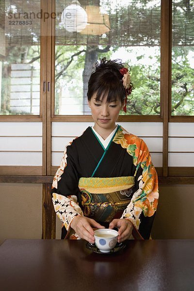 Eine Frau  die Kimono trägt und Tee trinkt.