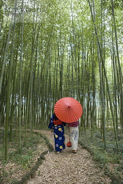 Zwei Frauen mit Kimonos  die durch einen Bambushain gehen.