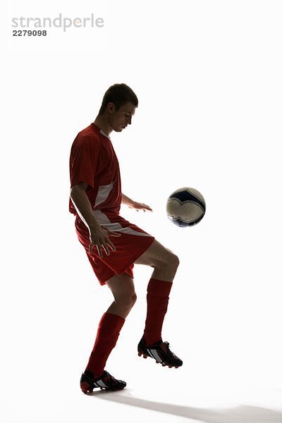 Studioaufnahme eines Fußballspielers  der einen Fußball auf sein Knie prallt.