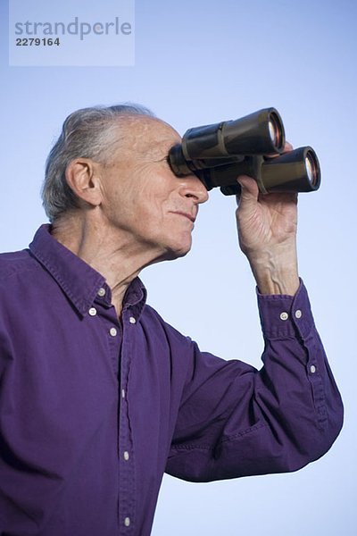 Ein älterer Mann  der ein Fernglas benutzt.