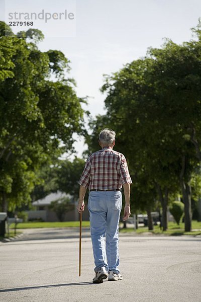Ein älterer Mann  der eine Straße entlanggeht.
