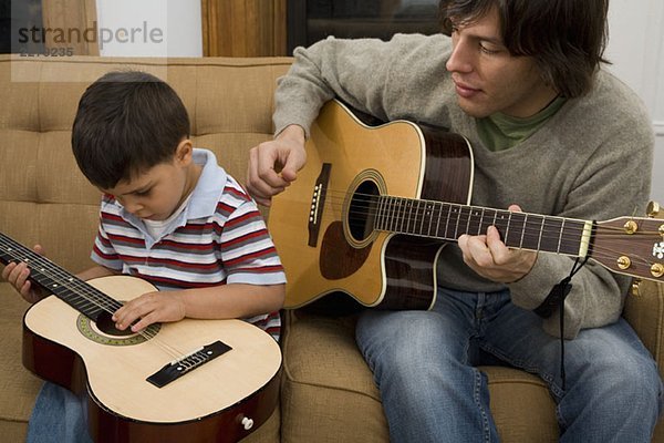 Ein Mann und ein Junge spielen zusammen Gitarre.