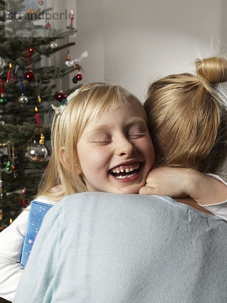 Ein Mädchen  das eine Frau neben einem Weihnachtsbaum umarmt.