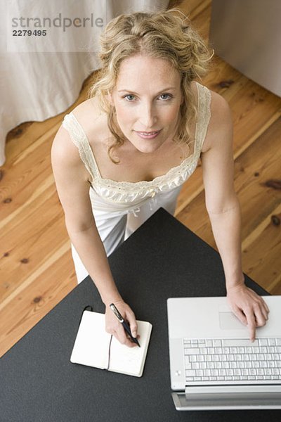 Eine Frau  die in ein Notizbuch schreibt und einen Laptop benutzt.