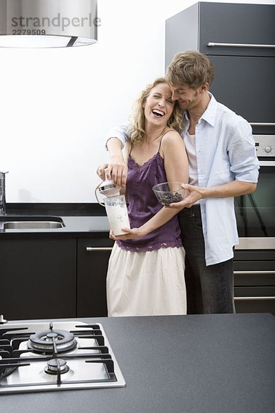 Ein erwachsener Mann mit den Armen um eine erwachsene Frau  die einen elektrischen Mixer hält.