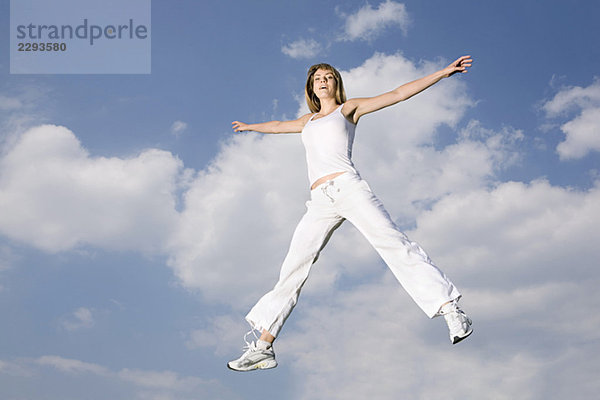 Junge Frau springt in der Luft  Arme ausgestreckt  lächelnd